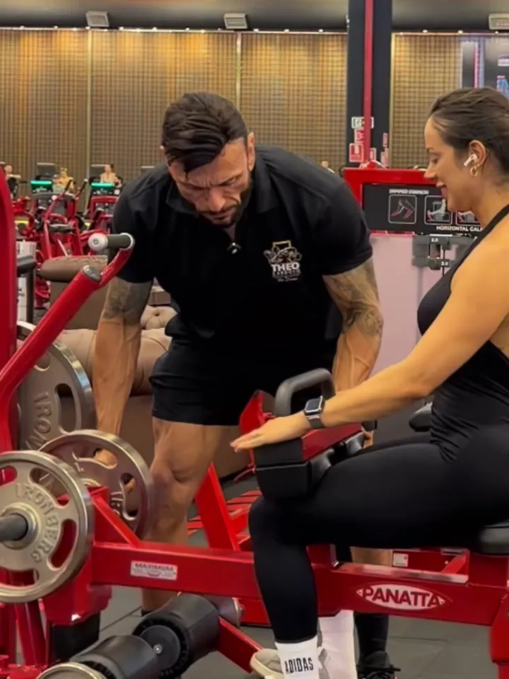 Théo ao lado de uma aluna na panturrilha sentada, ajustando a posição dela na máquina